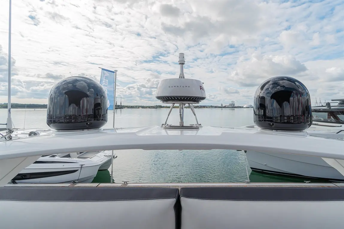 View from a yacht showing two black radar domes and a white Quantum2 unit, with boats docked and clouds reflecting on water.